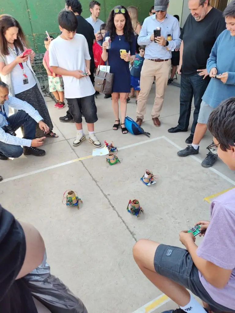 Familias observando a sus hijos controlar walker_bots en el patio del edificio de ingeniería